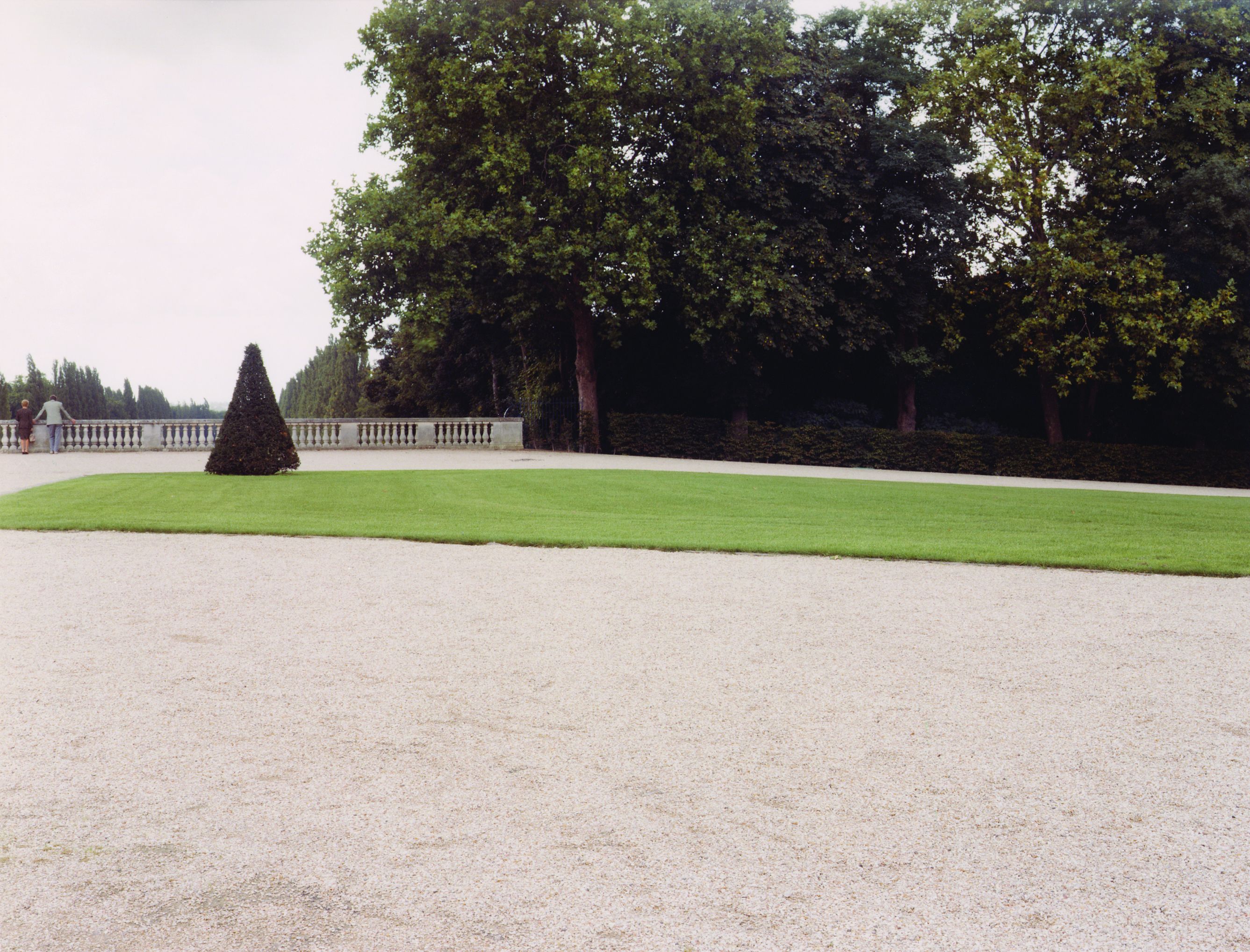 A photo of a park. You can recognise a lawn and a pebble path. A couple can also be recognised in the distance.