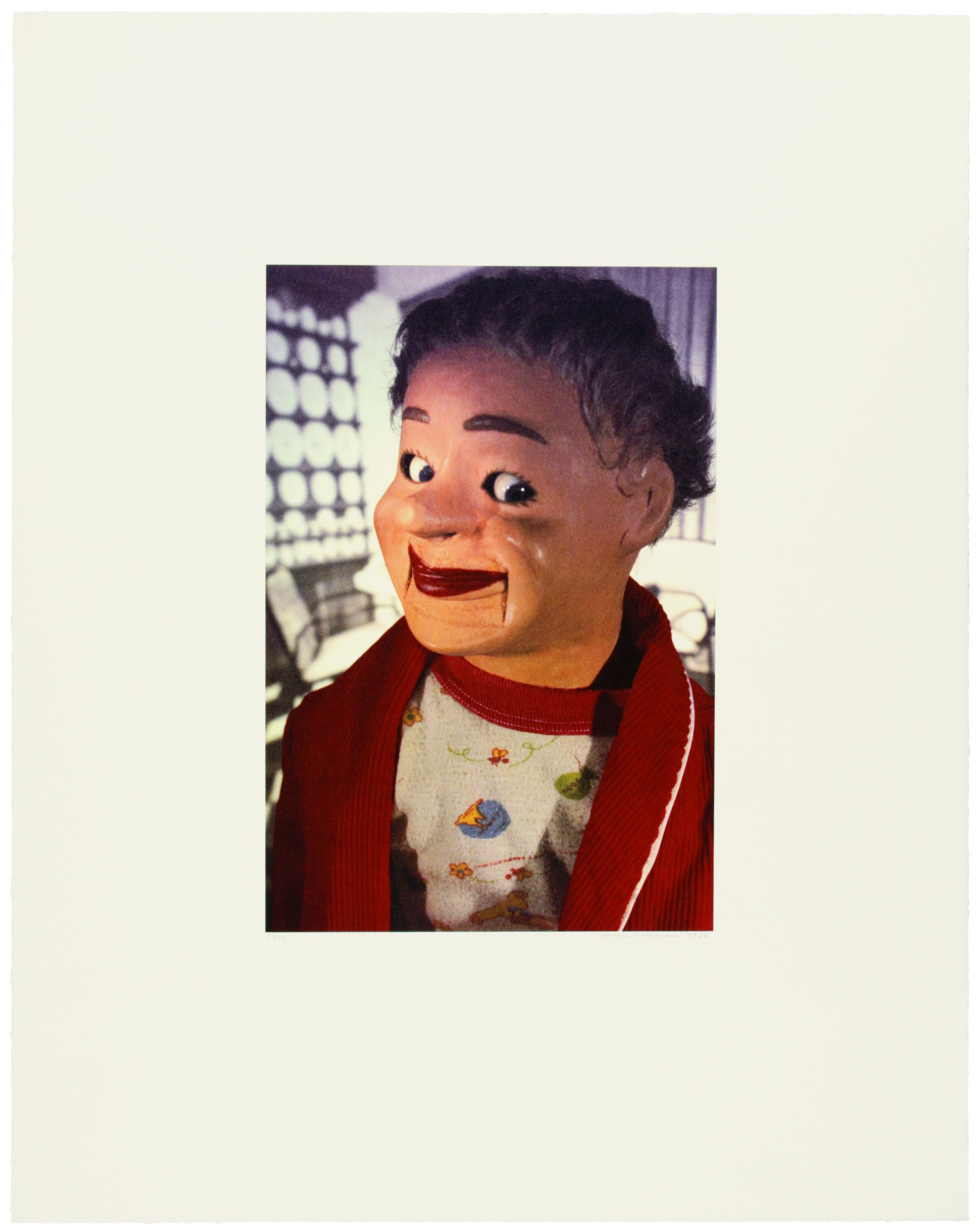 Auf dem Bild ist eine Puppe. Das Bild ist farbig. Die Puppe schaut in die Kamera. 