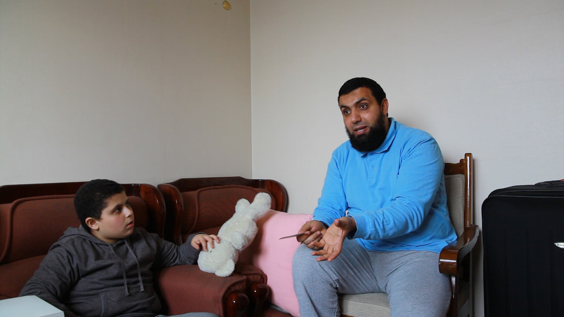 A photo of a man with a beard and a child. The man is sitting on a chair and the boy in an armchair or on a sofa.
