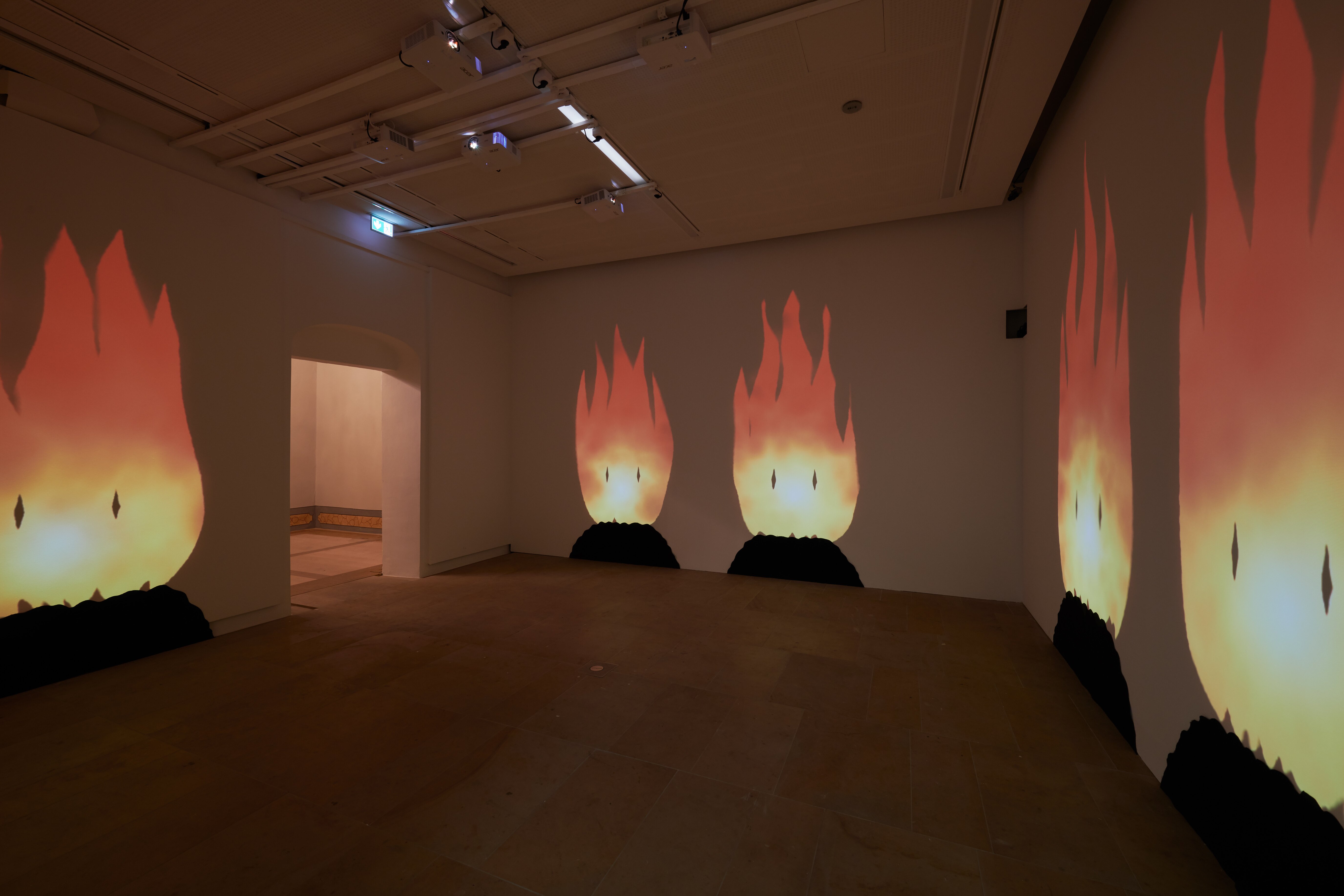 Darkened room with large projections of comic-like fires with faces reaching from the floor almost to the ceiling