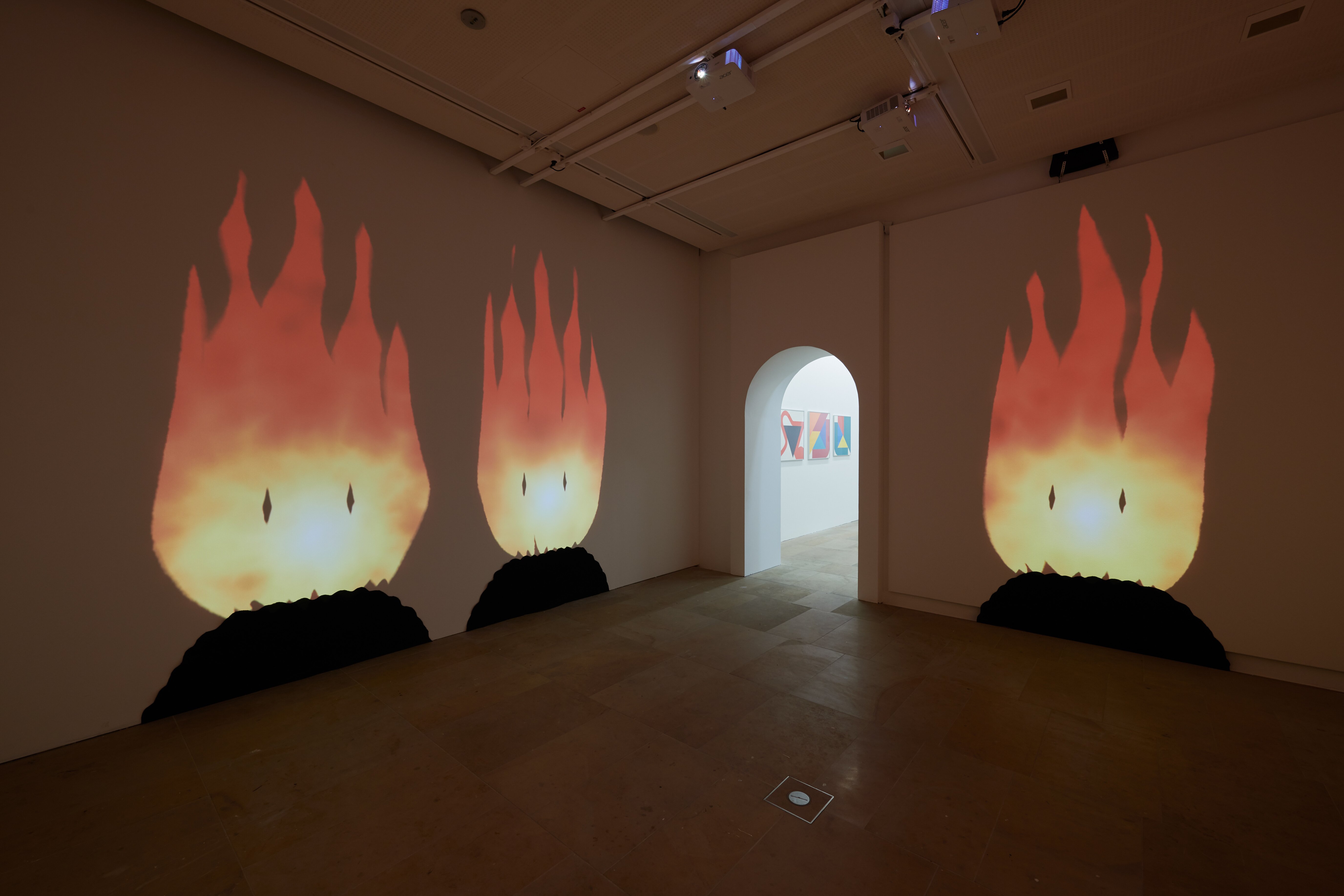 Darkened room with large projections of comic-like fires with faces reaching from the floor almost to the ceiling