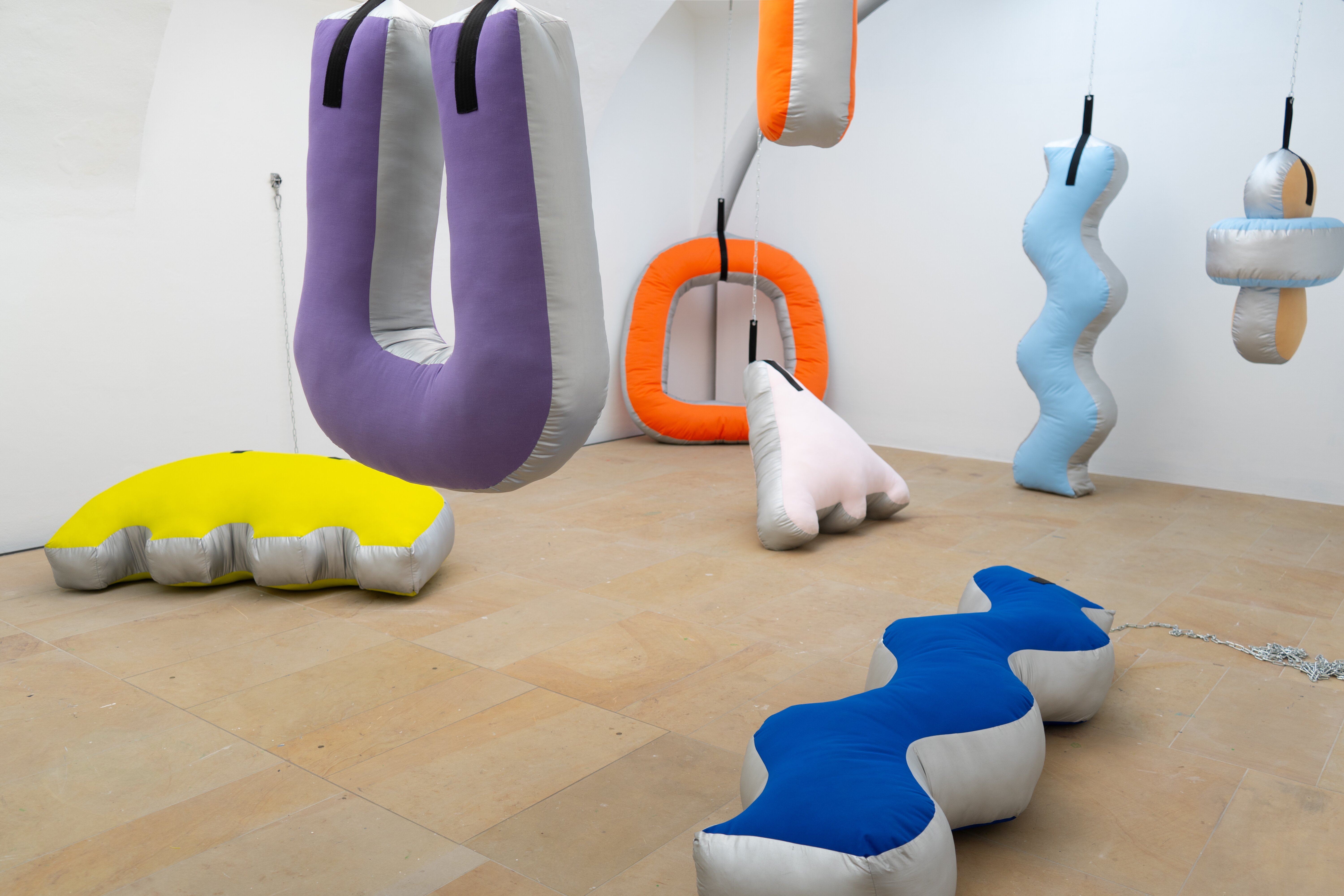 Large colorful fabric sculptures in a white room, some lying on the floor or hanging from the ceiling