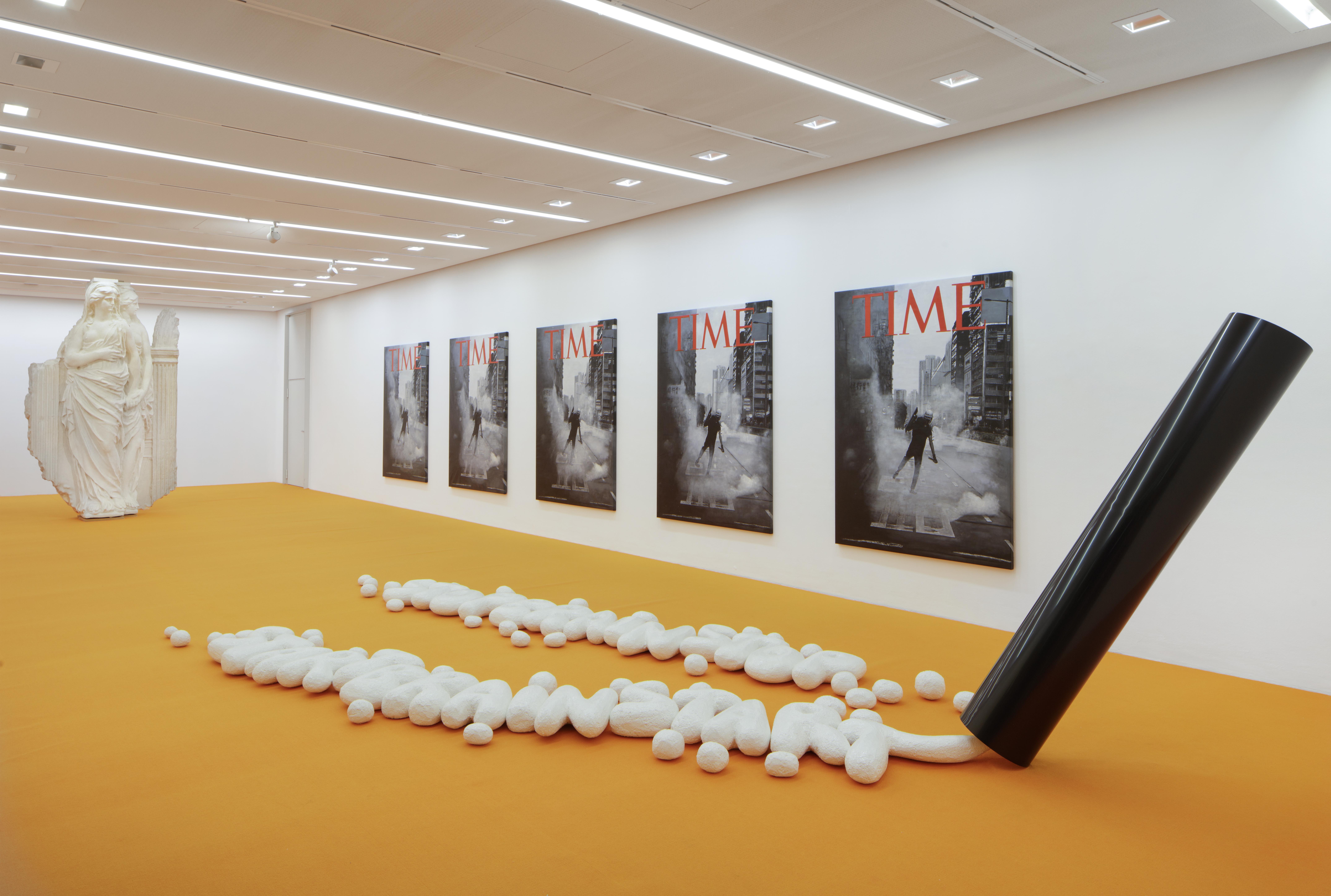 Bild einer Ausstellung mit Postern an der Wand und einer Installation auf dem Boden und einer Skulptur.
