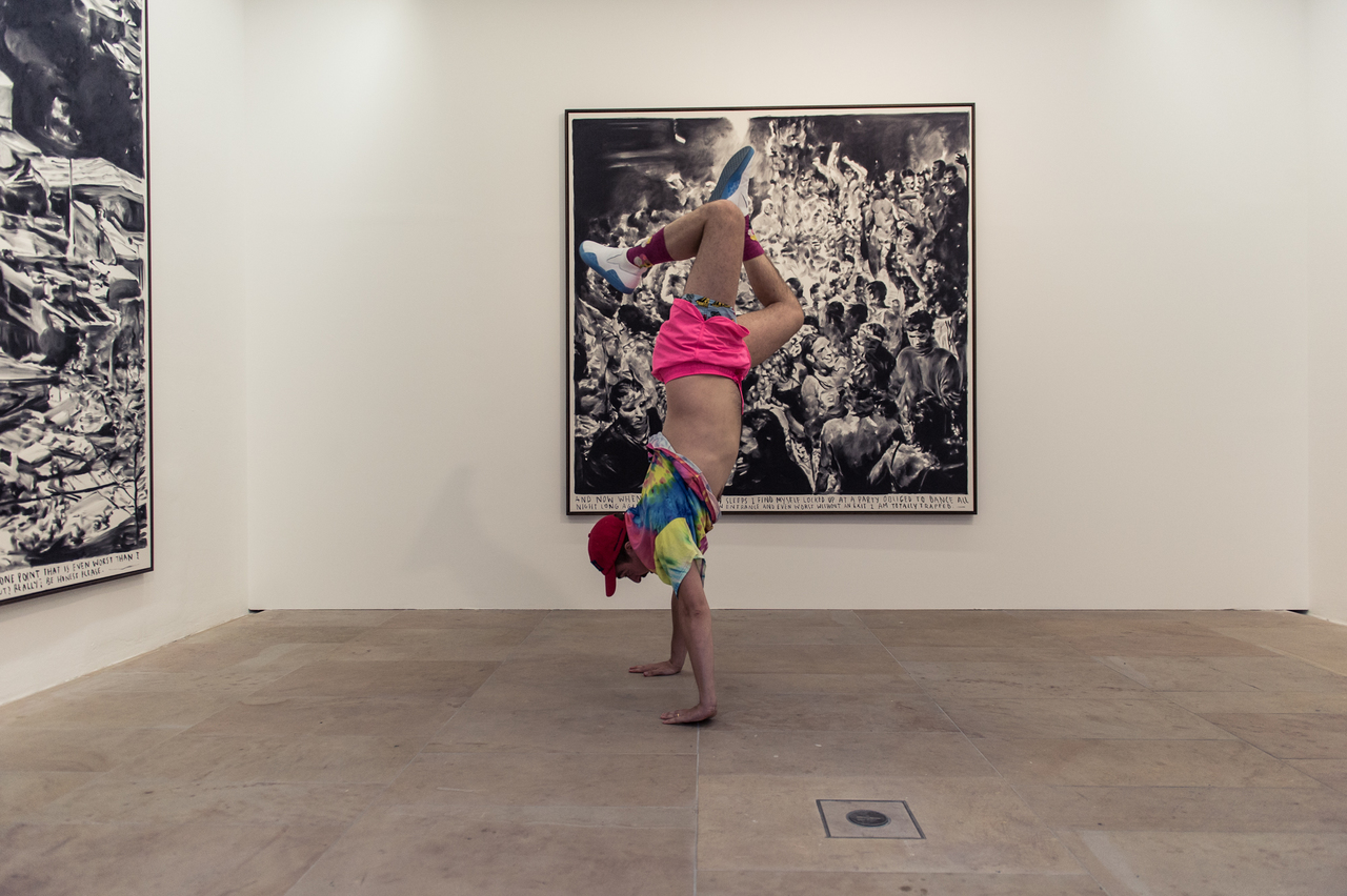 A visitor does a handstand in front of the large-scale charcoal drawings by artist Rinus van de Velde.